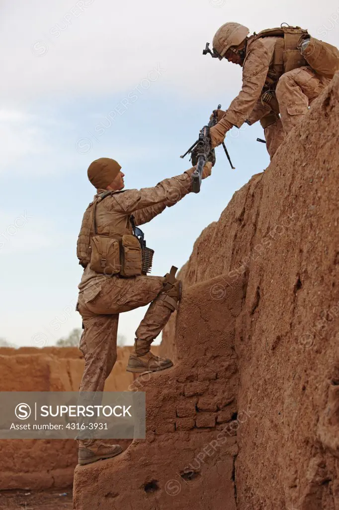 A U.S. Marine Hands an M249 Squad Automatic Weapon, or SAW, to Another Marine Atop a Roof of an Abandoned Farm House During a Combat Operation in Afghanistan's Helmand Province