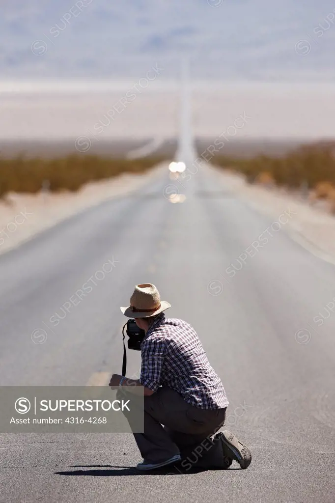 Woman in Middle of Desert Highway Photographing Approaching Car and Inferior Mirage