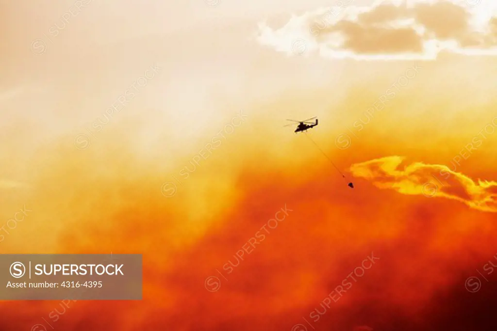 Helicopter With Helicopter Water Bucket For Fire Fighting, Flying Through Smoke of Wildfire