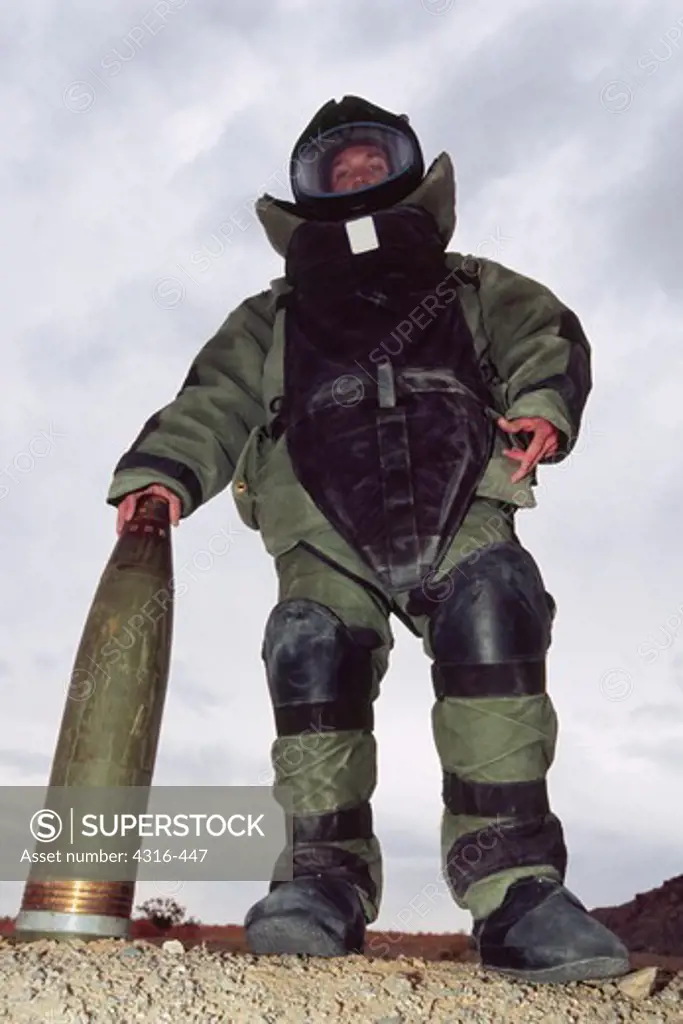 A US Marine Explosive Ordnance Disposal Specialist in a Bomb Disposal Suit Palms the Tip of a 155mm High Explosive Artillery Round