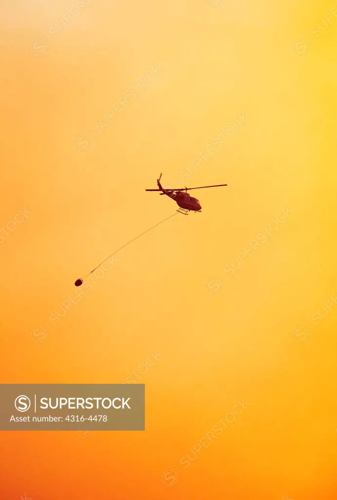 Firefighting helicopter carrying a bucket of water to a raging mountain wildfire, Colorado, USA
