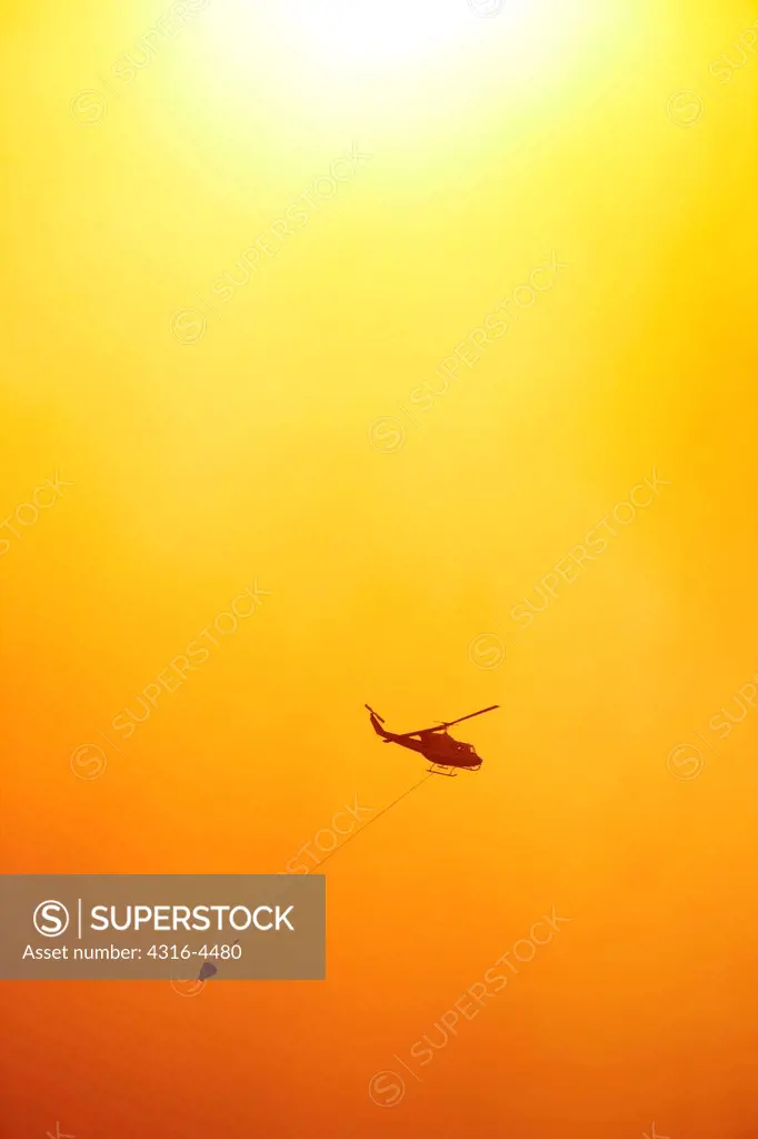 Firefighting helicopter carrying a bucket of water to a raging mountain wildfire, Colorado, USA