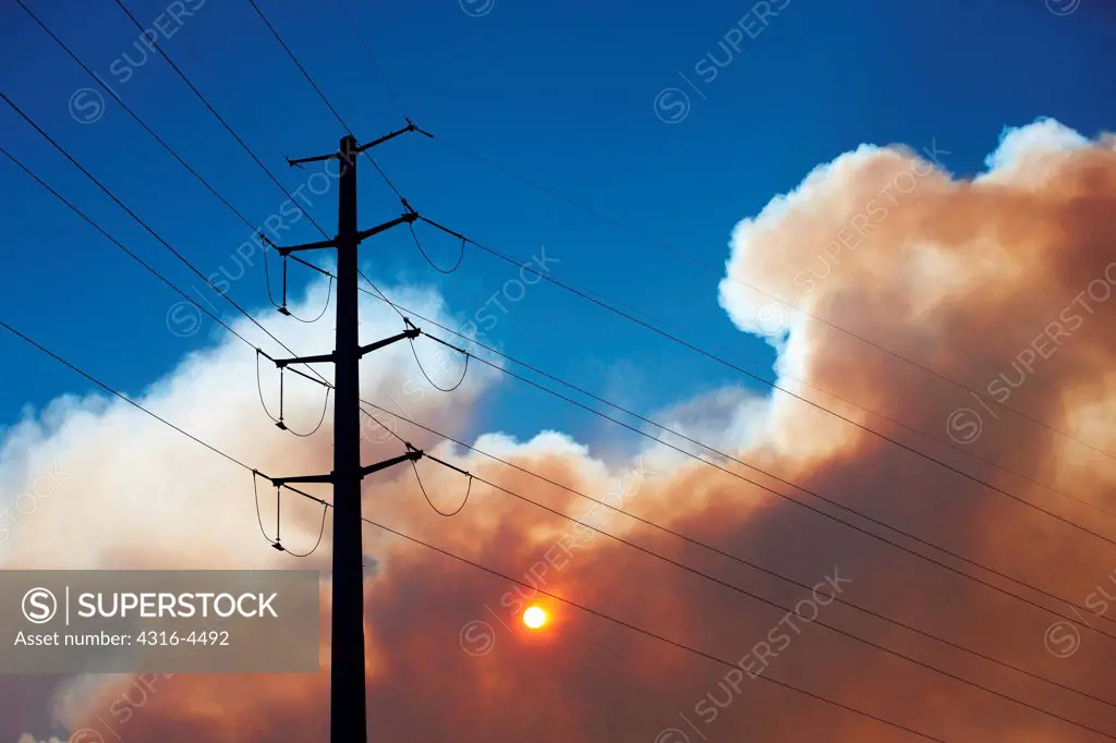 High voltage power lines, sun, and plume of smoke from raging Colorado wildfire, Colorado, USA