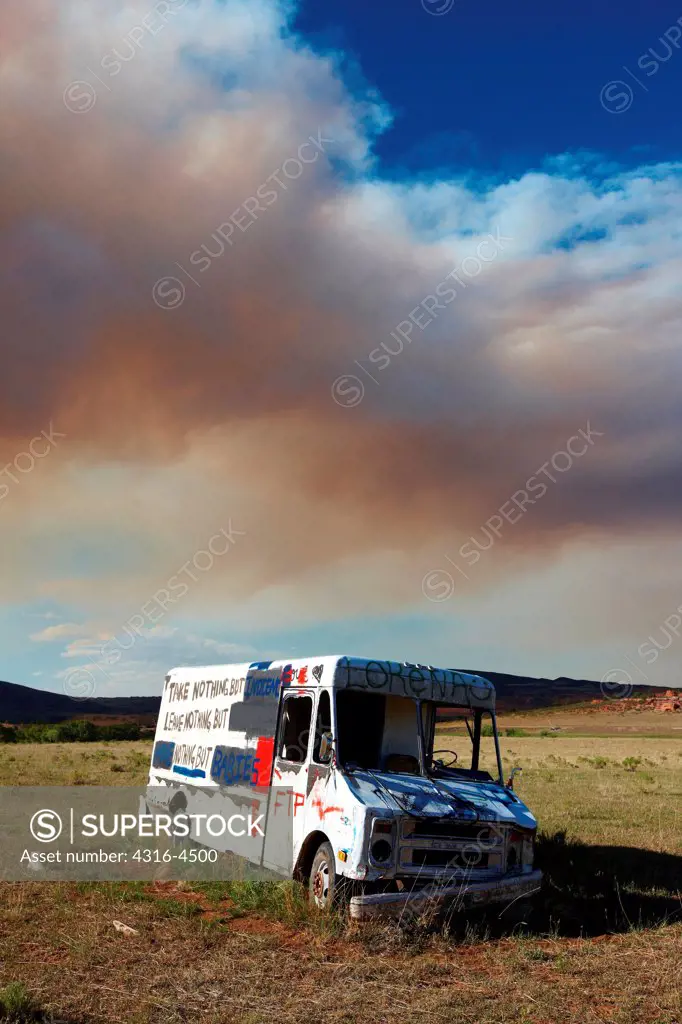 Abandoned delivery truck, plume of smoke from raging mountain wildfire, Colorado, USA