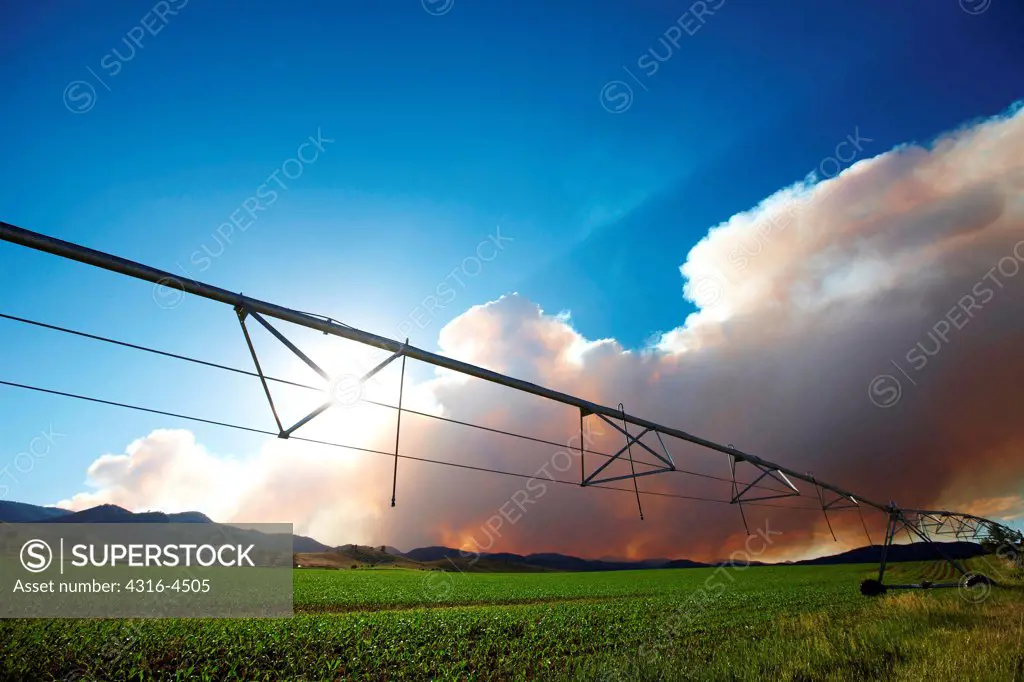 Plume of smoke rises from raging mountain wildfire, foreground center-pivot irrigation system, Colorado, USA