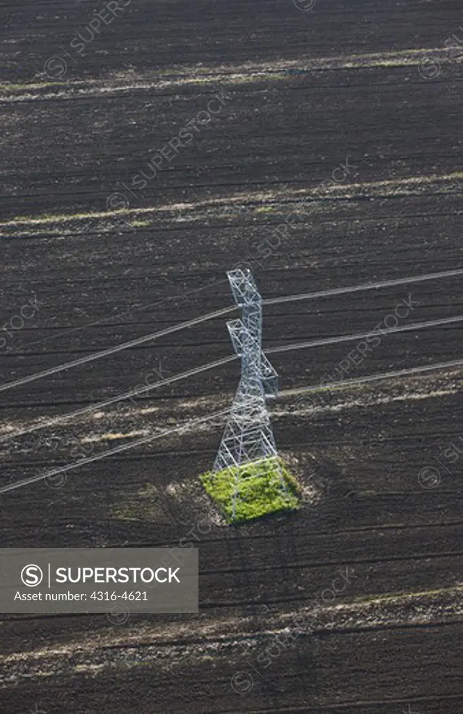 Aerial view of high voltage power lines, a power line tower, and an agriculture field, California