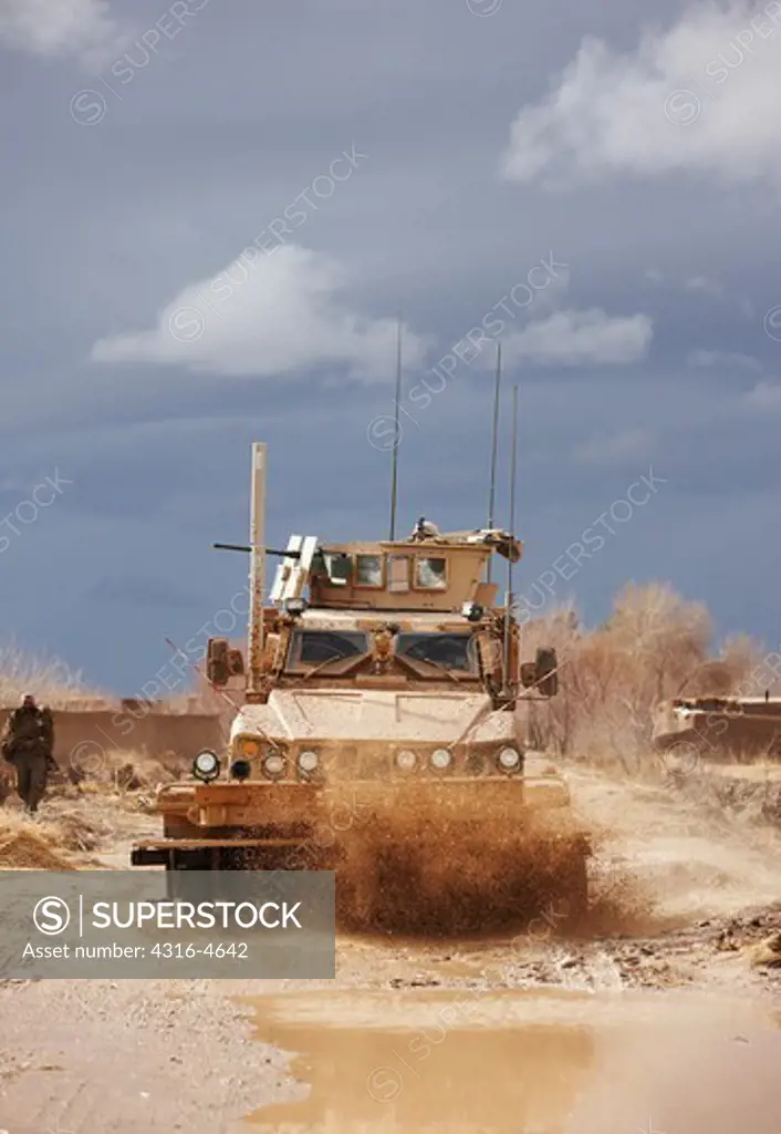 M-ATV, or Mine Resistant, Ambush Protected, All Terrain Vehicle, with a mine roller fitted to it, drives through puddles on a muddy dirt road in Afghanistan's Helmand Province