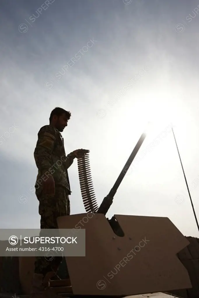 Silhouette of Afghan National Army soldier loading a belt of .50 caliber bullets into an M2 machine gun, Helmand Province of Afghanistan