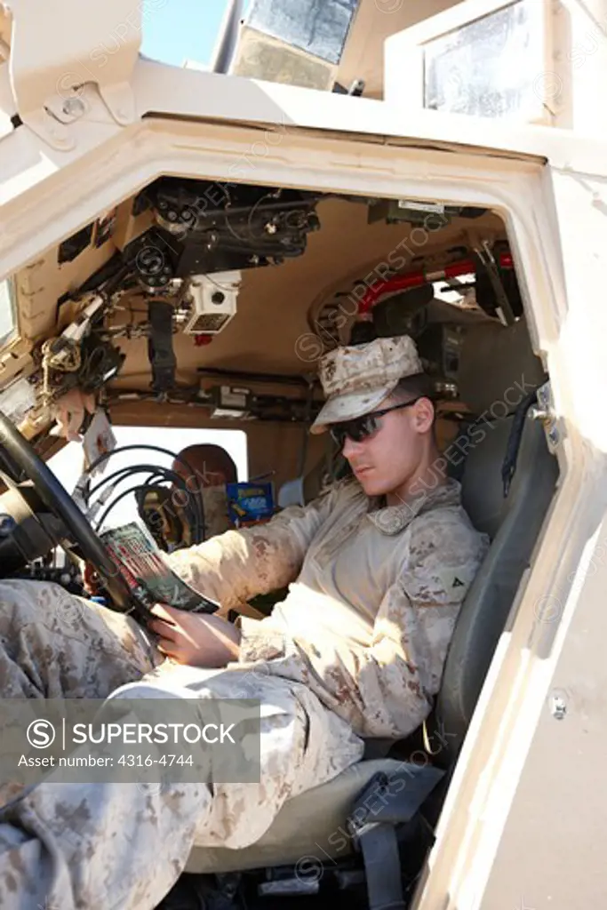 A United States Marine reads a book from the cab of an MRAP, or Mine Resistant, Ambush Protected Vehicle, Helmand Province of Afghanistan