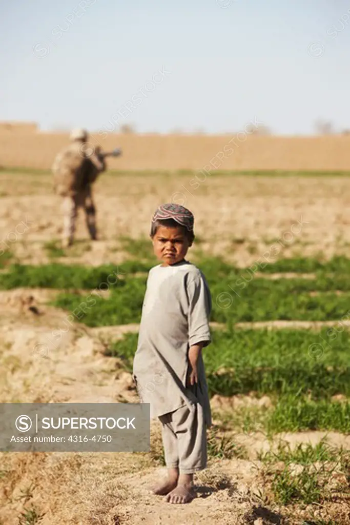 Afghan boy in field with U.S. Marine in distance during combat operation in Afghanistan's Helmand Province