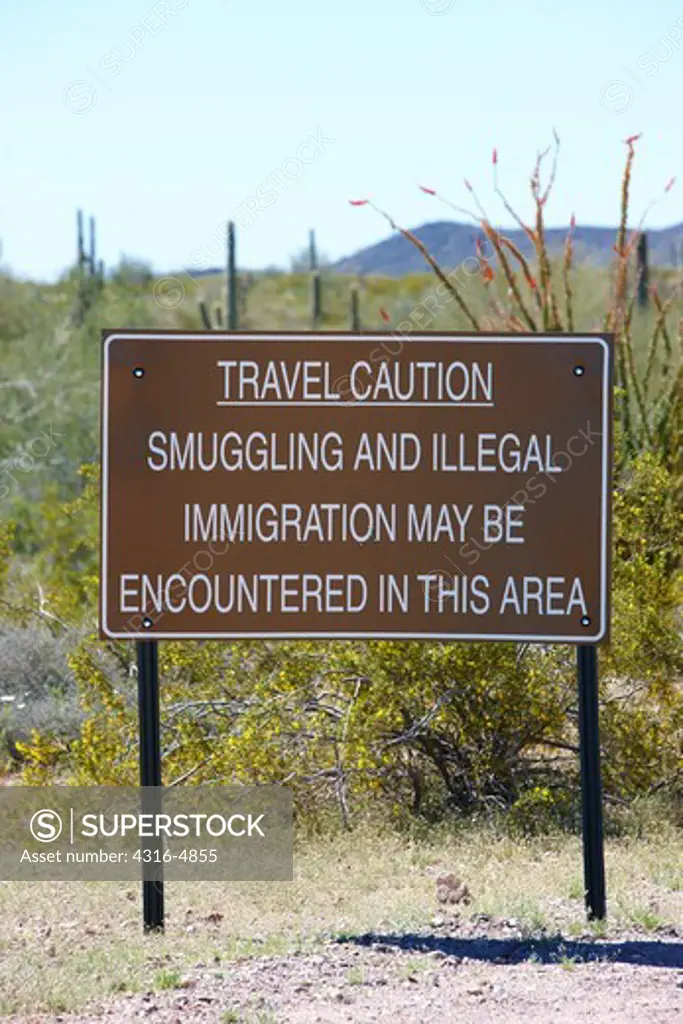 Travel caution sign in desert of southern Arizona near border with Mexico, warning of smuggling and illegal immigration
