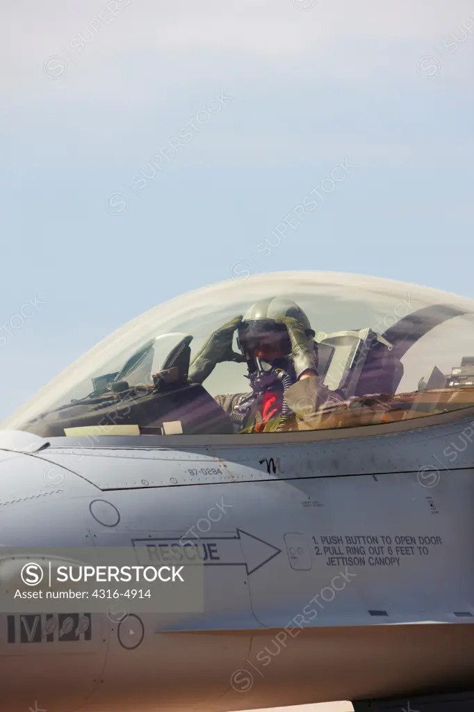 Fighter pilot in cockpit of F-16, adjusting visor of helmet