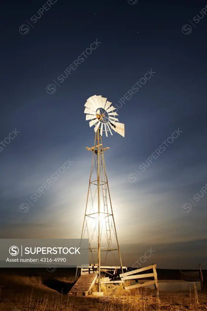 Windmill on plains at night, backlit by moon