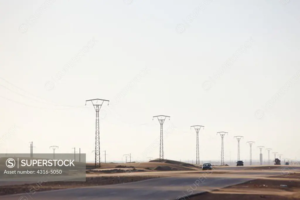 Sheets of sand blow across highway and around high voltage power lines and power poles, near Laayoune, Western Sahara, north Africa