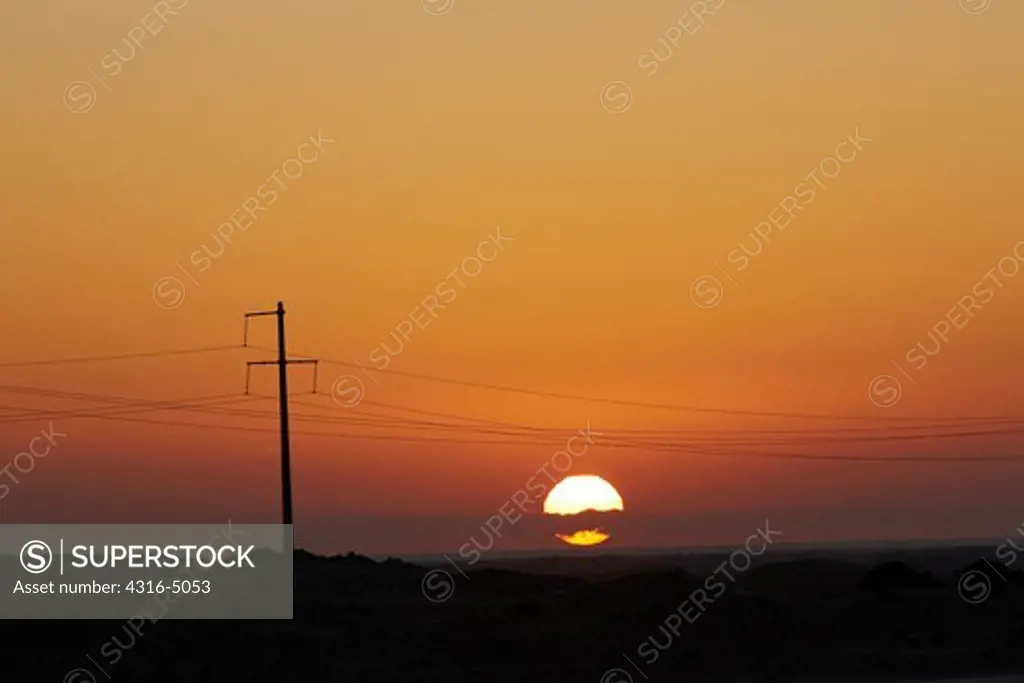 Setting sun silhouettes high voltage power lines and power line pole, near Laayoune, Western Sahara, North Africa