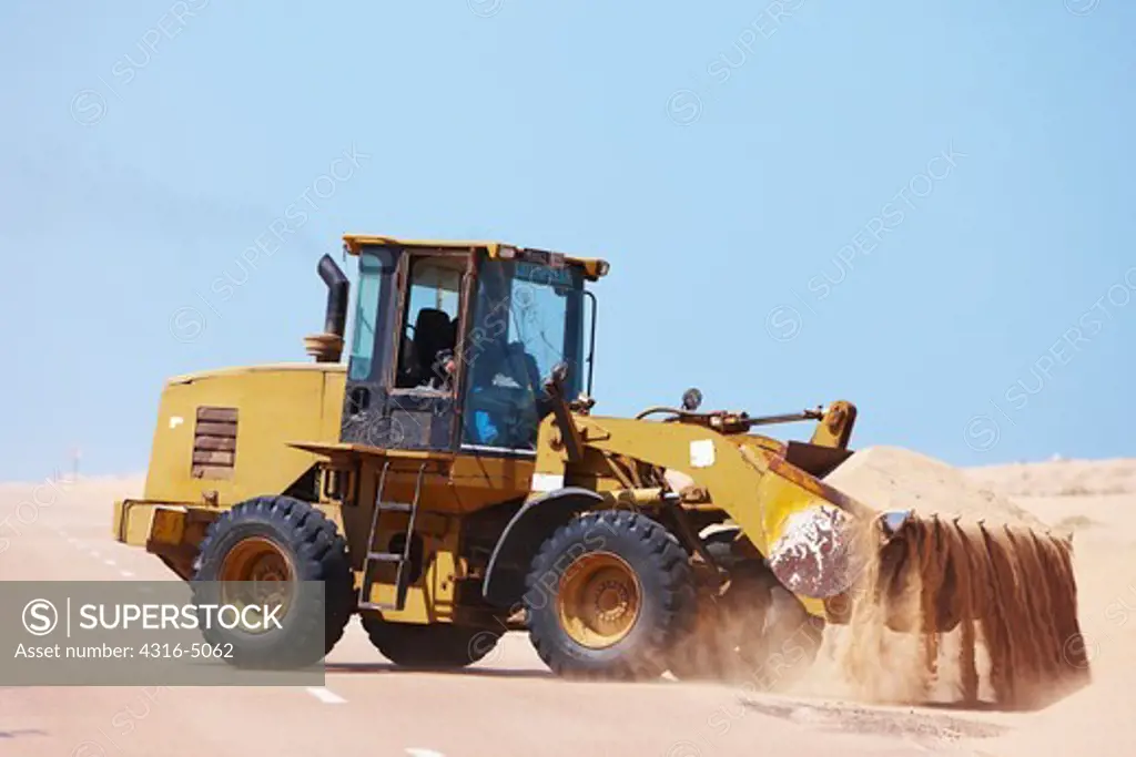 Front end loader removing accumulated sand from roadway, southern Morocco