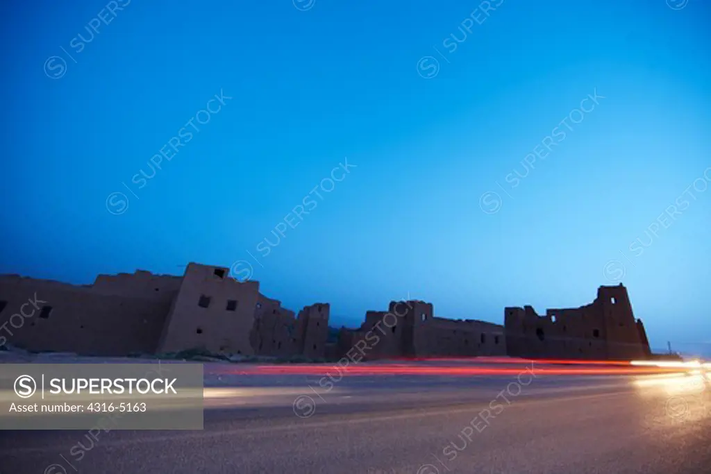 Ruins of earthen dwellings, modern paved road, light streaks of passing vehicles, Morocco