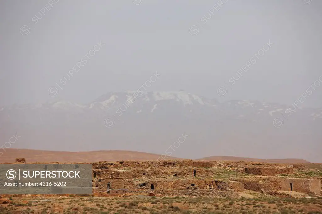 Ruins of stone buildings in foreground snow capped peaks of high Atlas Mountains in background, Sahara Desert, Morocco