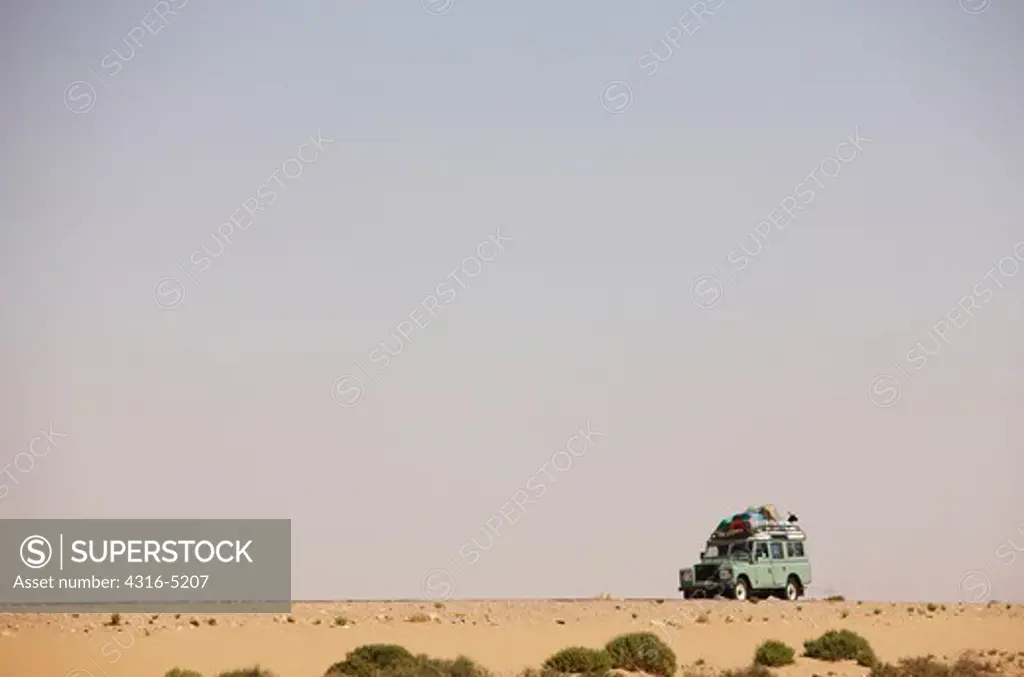 Bedouin nomads in Land Rover, with all their possessions, including a goat tied to the roof, southern Morocco, Sahara Desert at the Atlantic Coast