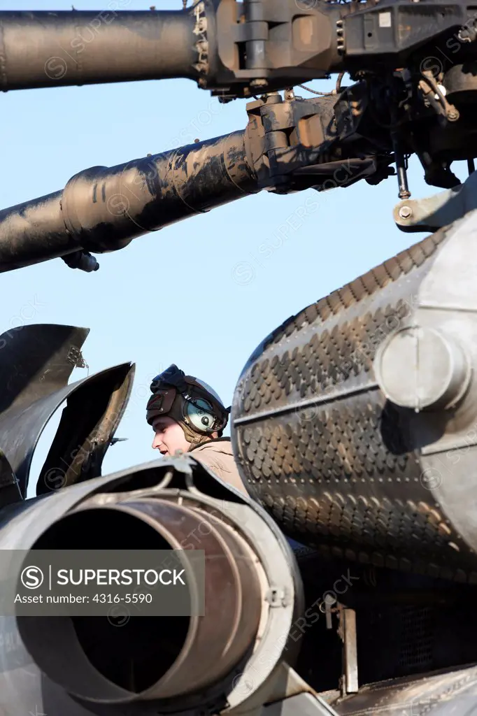 United States Marine aircraft maintenance specialist works on a CH-53E Super Stallion heavy lift helicopter, with exhaust of one of the helicopter's three engines and EAPS, or Engine Air Particle Separator in frame, Helmand Province, Afghanistan