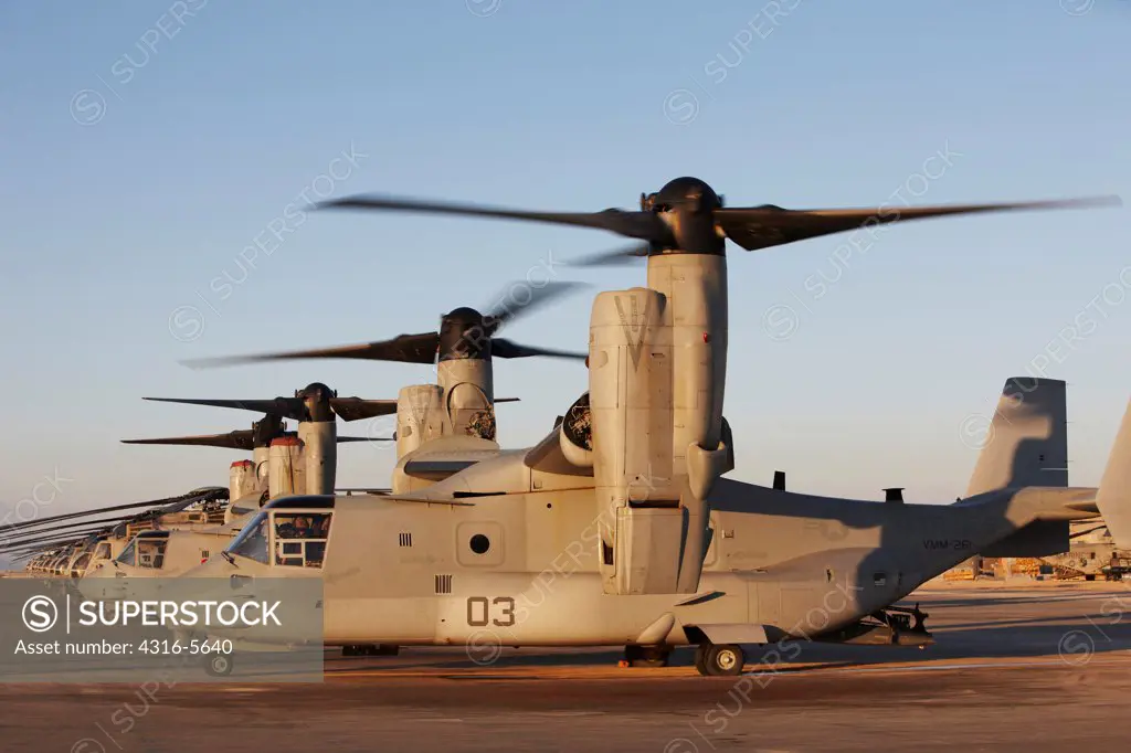 United States Marine Corps MV-22 Osprey, with proprotors spinning, prepares to depart on a mission from Camp Bastion, Helmand Province, Afghanistan, line of other MV-22 Ospreys and CH-53 heavy lift helicopters in background