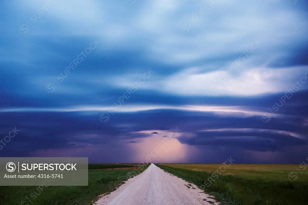 USA, Oklahoma, Dirt road disappears in distance below mesocyclone