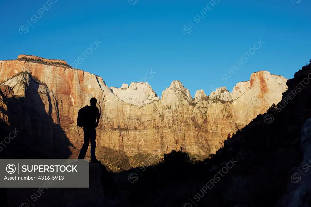 USA, Utah, Hiker silhouetted by morning light on amphitheater of stone, Zion National Park