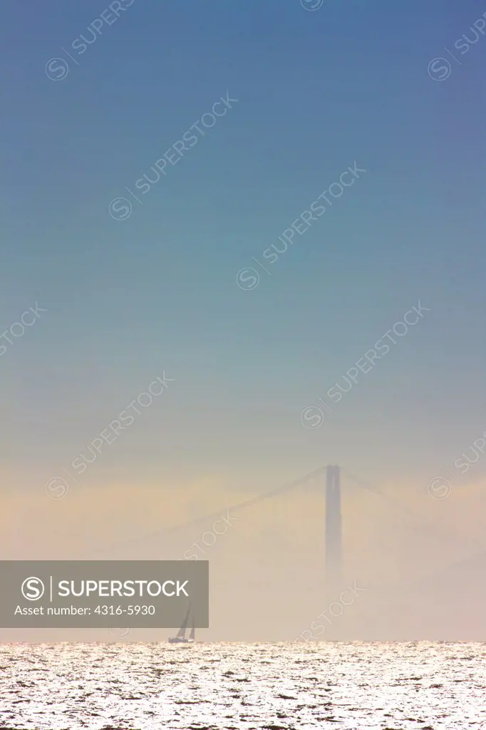 USA, California, Distant sailboat passes by north tower of Golden Gate Bridge, obscured by fog in San Francisco Bay