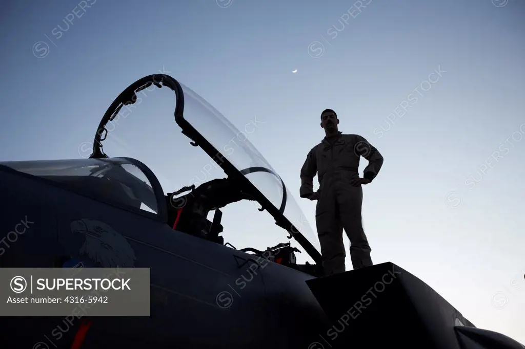 Afghanistan, Bagram, Bagram Airfield, Silhouette of United States Air Force F-15E Strike Eagle pilot standing atop nose of F-15 by cockpit