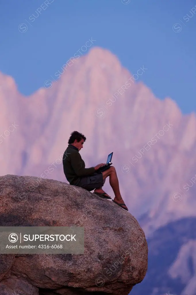 USA, California, Man using laptop atop boulder rock with Mount Whitney in background