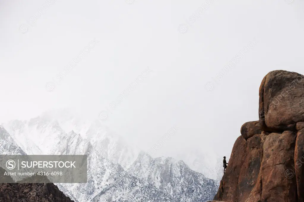 USA, California, Alabama Hills, Hiker climbing large boulder with Sierra Nevada Peaks in background
