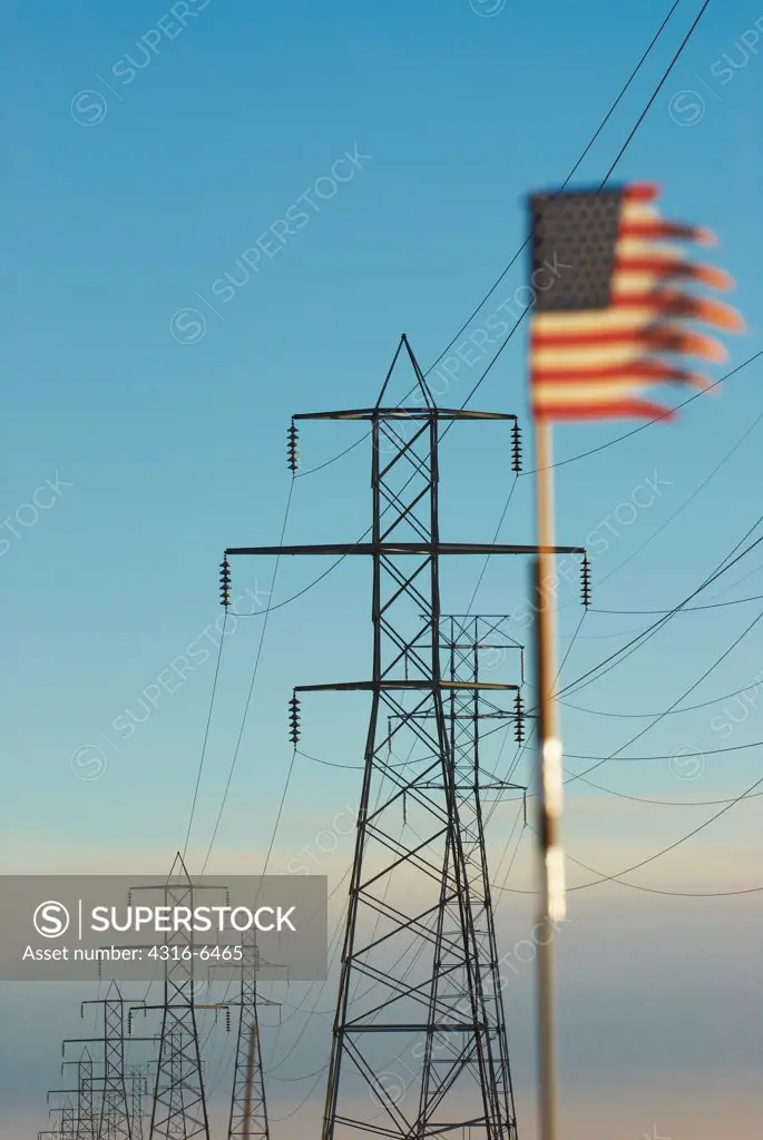 American flag tattered by high wind and high voltage power lines with smoke from raging wildfire in distance, San Bernardino County, California, USA