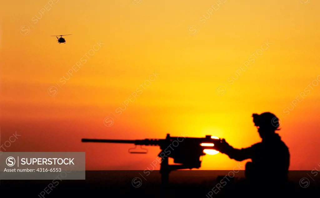 Silhouette of a US Marine manning an M2 .50 caliber machine gun and a US Marine Corps UH-1N Iroquois Utility Helicopter