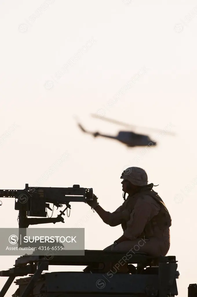 Silhouette of a US Marine manning an M2 .50 caliber machine gun and a US Marine Corps UH-1N Iroquois Utility Helicopter