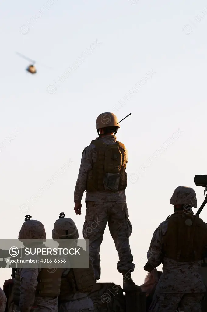 Silhouettes of US Marines on the ground directing a UH-1N Iroquois utility helicopter fitted with machine guns and rockets during live fire close air support training, Yodaville, Barry M. Goldwater Air Force Range, Arizona, USA