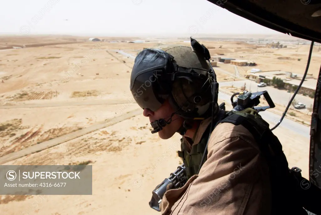 US Marine flight crew chief scans the desert below from a Marine Corps UH-1N utility helicopter fitted with weapons during combat operation launched out of Al Asad Air Base, Al Anbar Province, Iraq