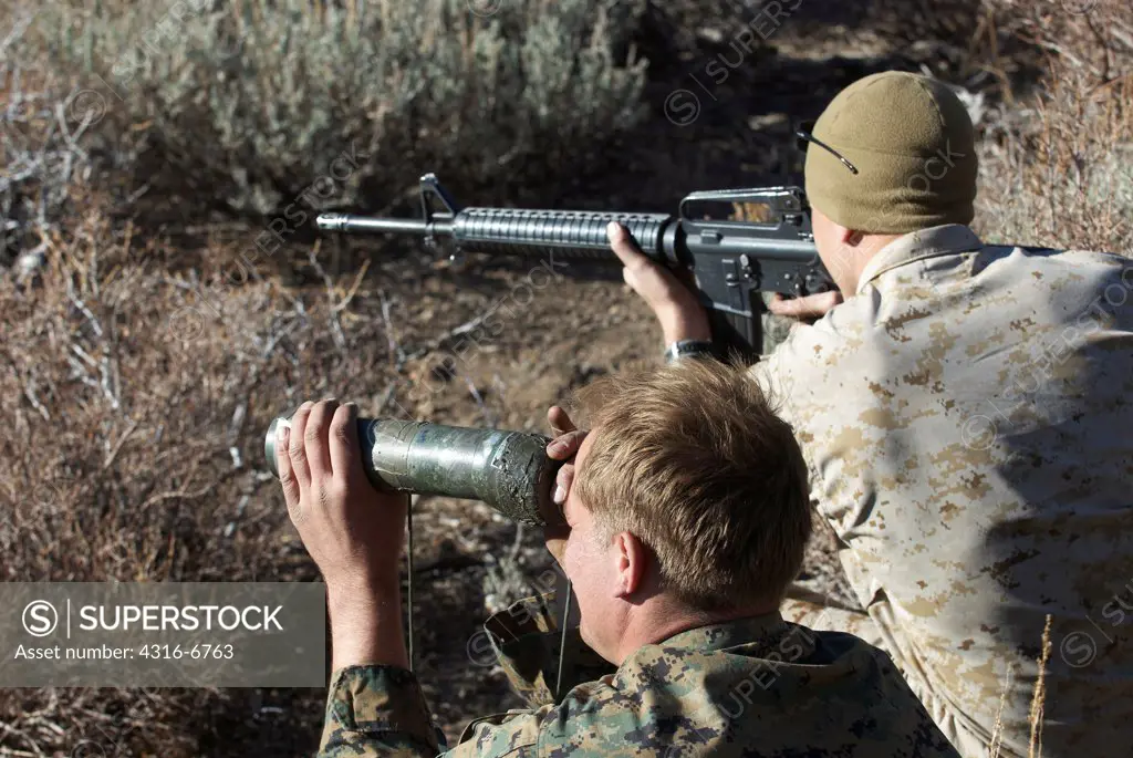 US Marine with the help of another Marine using a spotting scope aiming an M16 at a target during high angle mountain sniper training, Mountain Warfare Training Center, near Bridgeport, California, USA