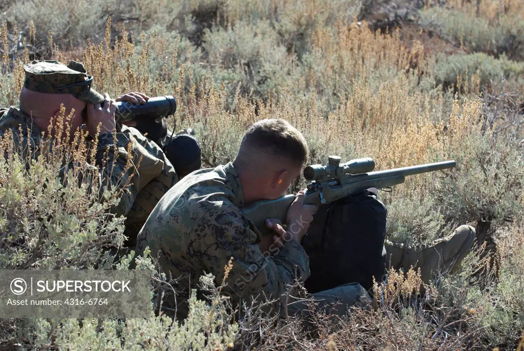 US Marine with the help of another Marine using a spotting scope aiming an M40A3 Sniper Rifle at a target during high angle mountain sniper training, Mountain Warfare Training Center, near Bridgeport, California, USA
