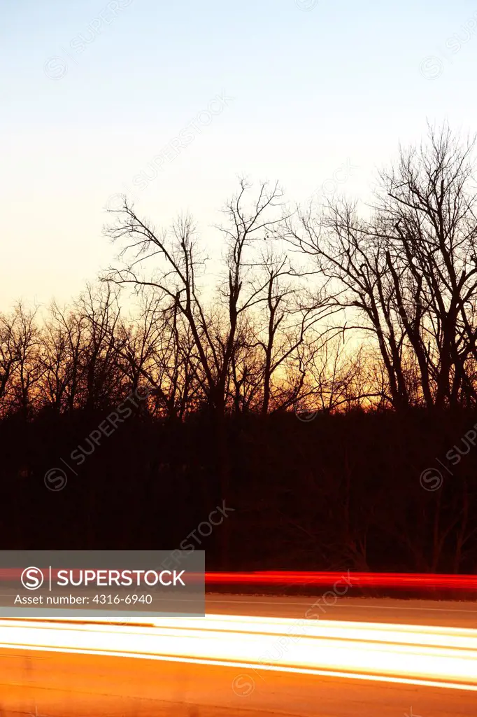 USA, Missouri, Car headlight and tail light streaks on road below forest at dusk