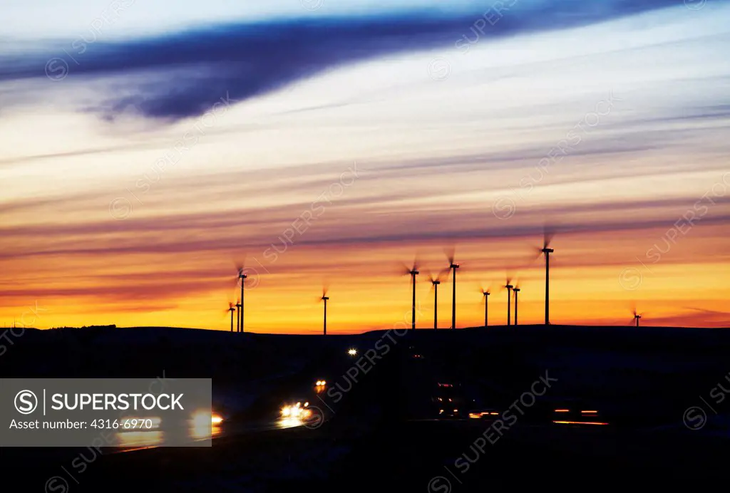 USA, Kansas, Streaks of lights of passing cars on Interstate highway and silhouettes of distant wind turbines of wind farm at dusk