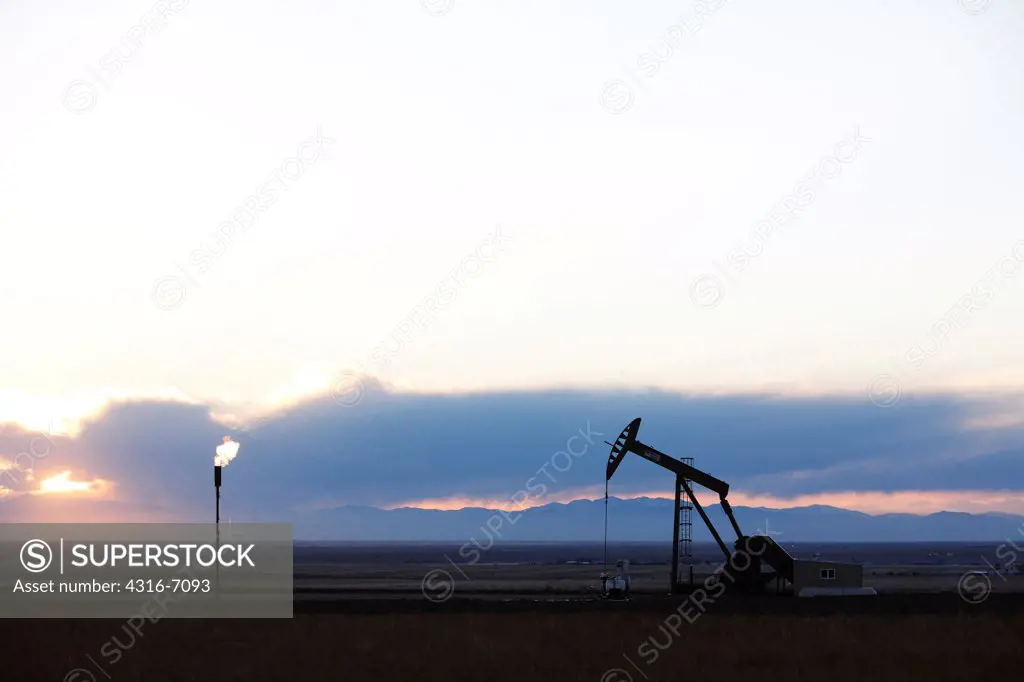 Oil well pumpjack and gas flare at sunset, eastern plains of Colorado, USA
