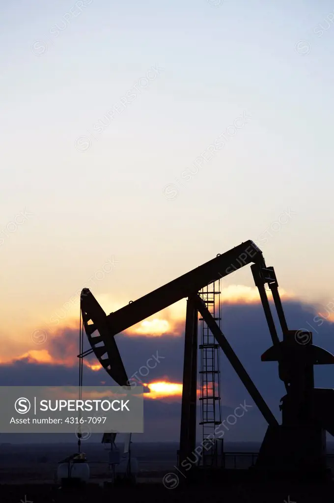 Oil well pumpjack at sunset, eastern plains of Colorado, USA
