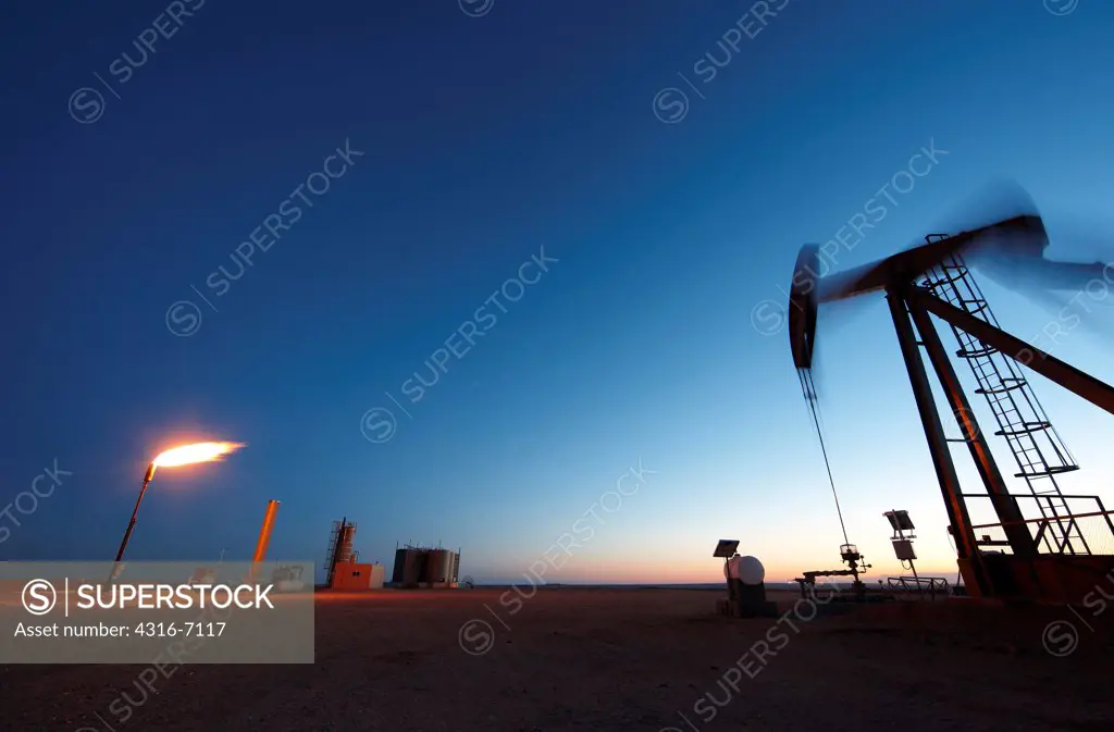 Oil well pumpjack and gas flare at dusk, eastern plains of Colorado, USA