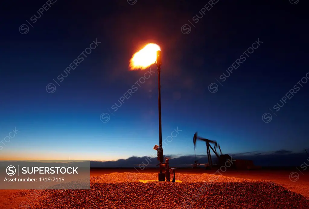 Gas flare with oil well pumpjack in background at dusk, eastern plains of Colorado, USA