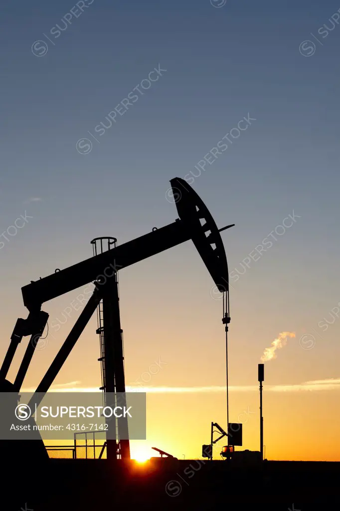 USA, Colorado, Oil well pumpjack (pump jack) and gas flare (flare stack), Oil well developed with hydraulic fracturing, also known as hydrofracking or fracking at Sunrise, diffraction of sun