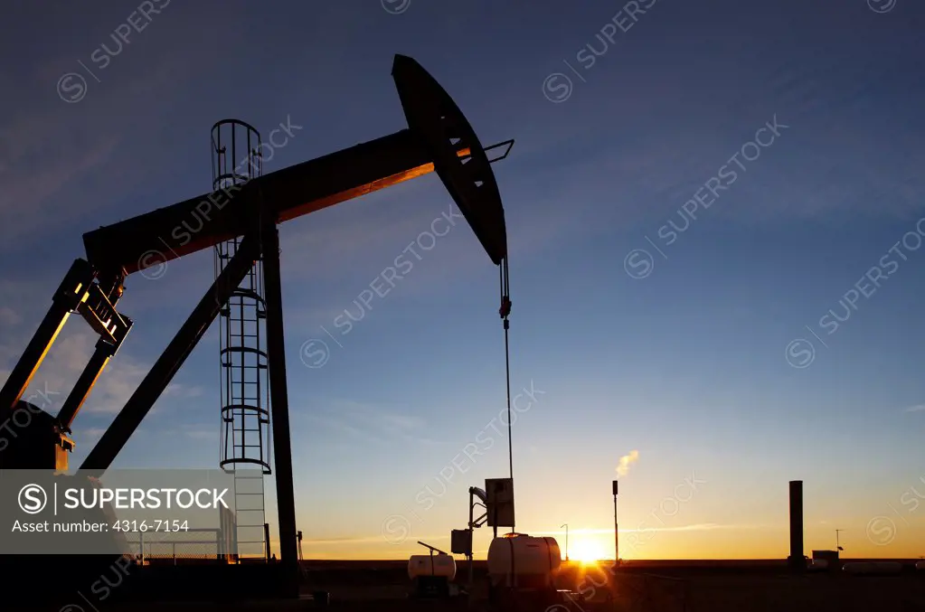 USA, Colorado, Oil well pumpjack (pump jack) and gas flare (flare stack) at sunrise