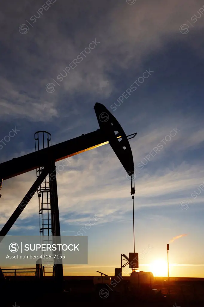 USA, Colorado, Oil well pumpjack (pump jack) and gas flare (flare stack) at sunrise