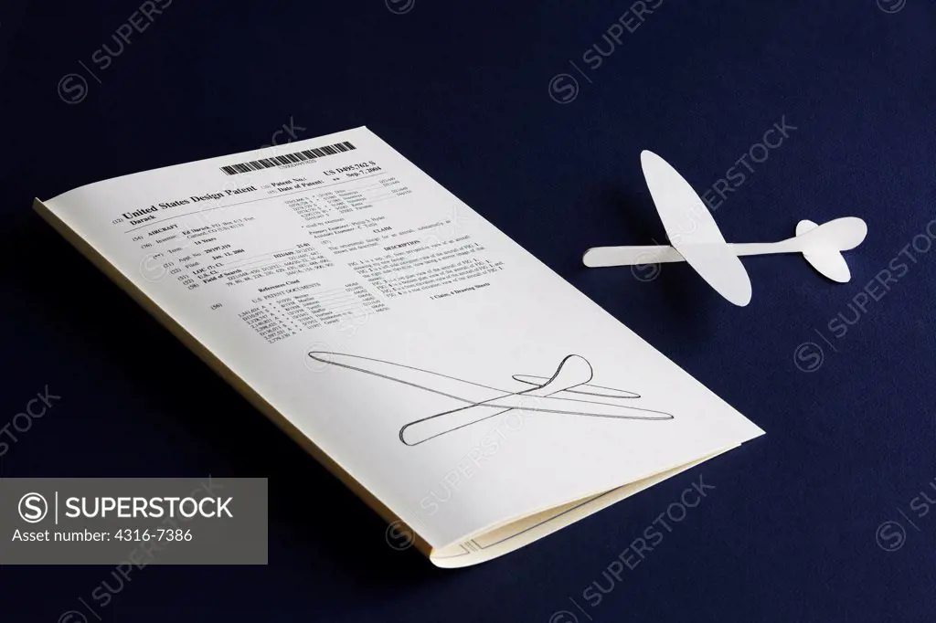 Small flying paperboard aircraft next to issued United States Patent for design of aircraft