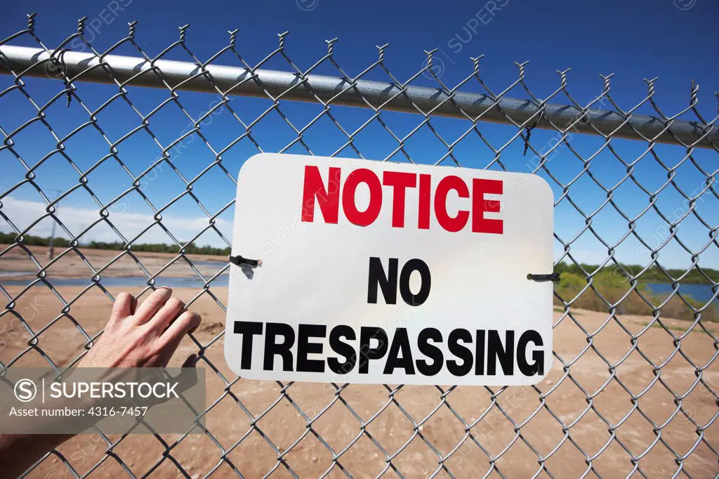 Man's hand clawing at fence with No Trespassing sign