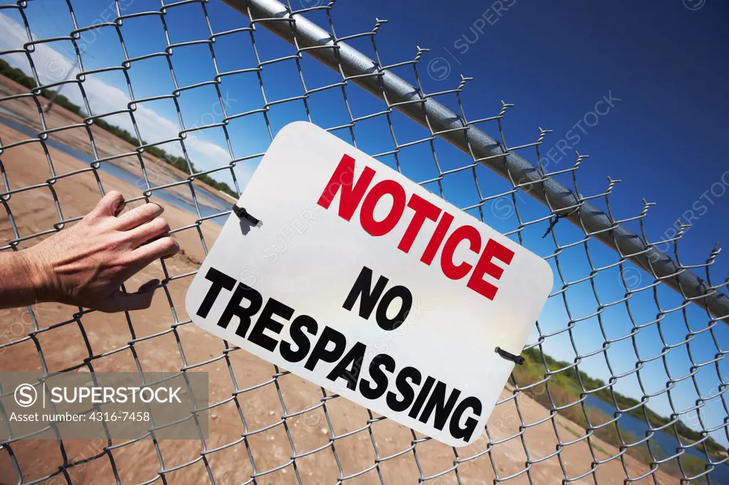 Man's hand clawing at fence with a No Trespassing sign